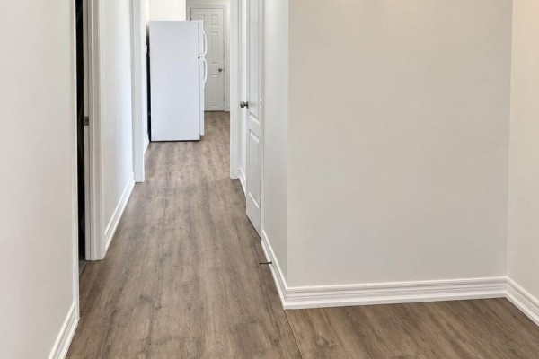 Hallway with white walls, grey wood-look flooring, and white doors leading to rooms. - Lower - 558 First Avenue, Welland