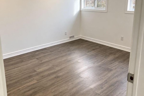 Bedroom with white walls, white baseboards, grey wood-look flooring, and two windows. - Lower - 558 First Avenue, Welland