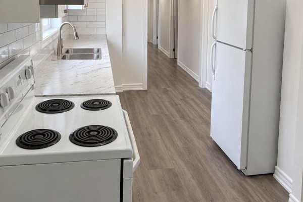 Kitchen area with white stove, double sink, white subway tile backsplash, and grey wood-look flooring. - Lower - 558 First Avenue, Welland