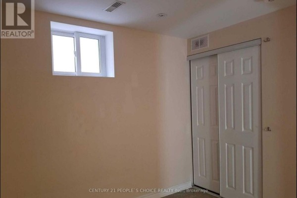 Empty basement room with peach walls, large sliding closet doors, and a window. - Lower - 5689 Sidmouth Street, Mississauga