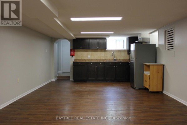 Empty basement living area with dark wood floors and archway to hallway. - Lower - 57 Carus Avenue, Toronto