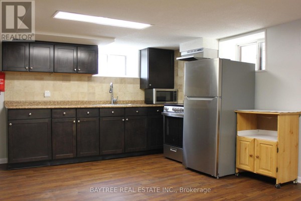 Basement kitchen with dark cabinets, granite counters, stainless steel fridge, and stove. - Lower - 57 Carus Avenue, Toronto