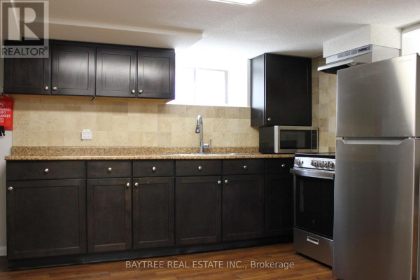 Close-up of basement kitchen cabinets, granite counter, tiled backsplash, and stainless steel appliances. - Lower - 57 Carus Avenue, Toronto
