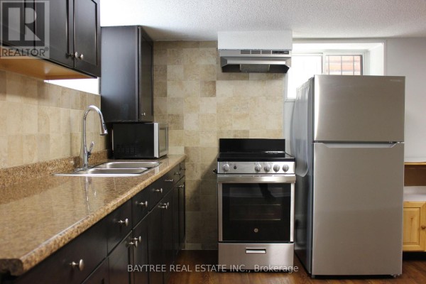 Basement kitchen sink, stainless steel stove, fridge, and microwave, with window view. - Lower - 57 Carus Avenue, Toronto
