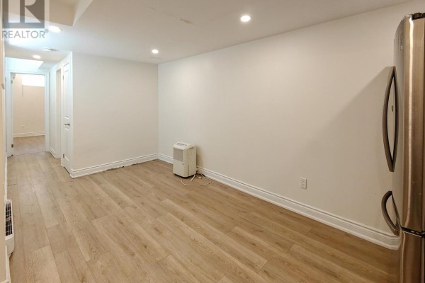 Living area with white walls, light wood floors, and a portable air conditioner. - Lower - 598 Crawford Street, Toronto