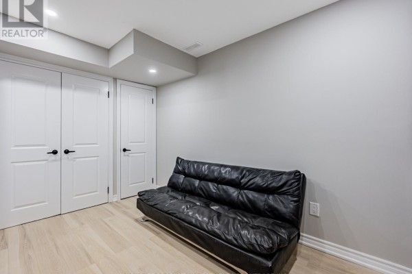 Basement room with light wood floors, grey walls, and a black futon sofa. - Lower - 6 Harper Hill Drive, Ajax
