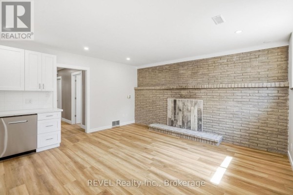 Living room with light wood floors, white cabinets, and brick fireplace. - Lower - 6166 Wildrose Crescent, Niagara Falls
