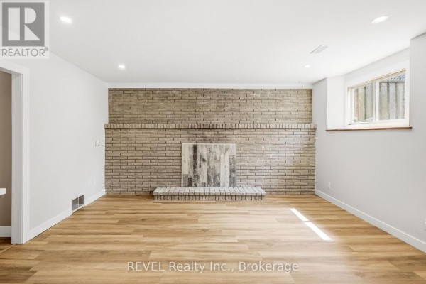 Empty living room with light wood floors and a large brick fireplace. - Lower - 6166 Wildrose Crescent, Niagara Falls
