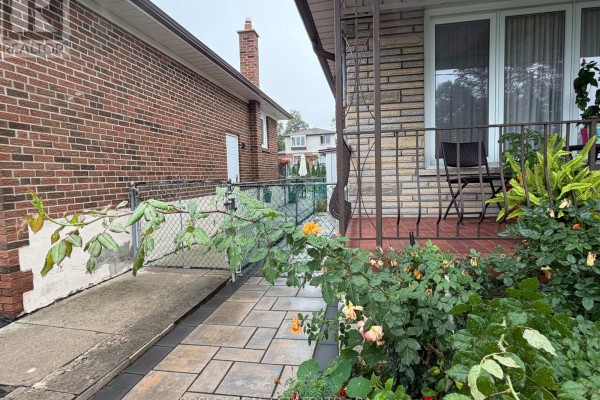 View of a brick house exterior with a chain-link fence and walkway with flowers. - Lower - 63 Ernest Avenue, Toronto