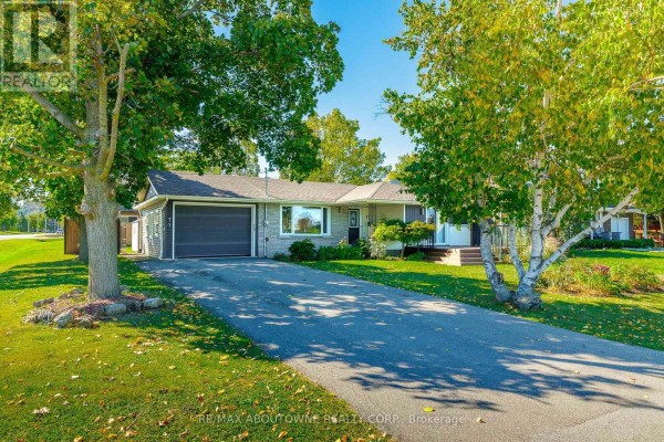View of the bungalow from the driveway, featuring a garage door and mature trees. - Lower - 71 Lakeside Drive, Grimsby