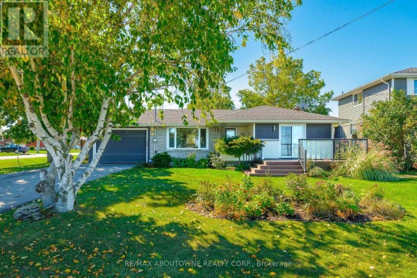 Side view of the bungalow with a manicured lawn, flower beds, and trees. - Lower - 71 Lakeside Drive, Grimsby
