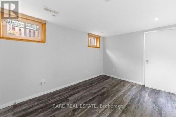 A vacant basement room with light gray walls, wood-look flooring, and two windows. - Lower - 733 Eaglemount Crescent, Mississauga