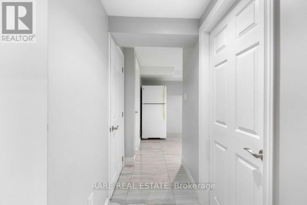 Interior hallway of a basement with white doors and a view of a white refrigerator at the end. - Lower - 733 Eaglemount Crescent, Mississauga