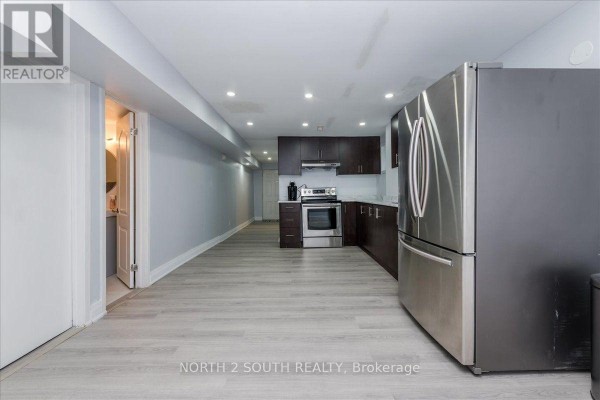 Long, narrow basement kitchen with dark wood cabinets, stainless steel appliances, and light gray floor. - Lower - 7520 Langworthy Drive, Mississauga