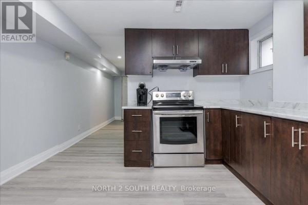 Corner view of a basement kitchen with dark wood cabinets and stainless steel stove. - Lower - 7520 Langworthy Drive, Mississauga