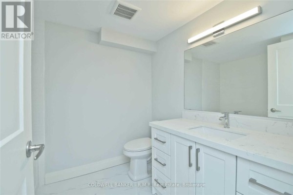 Modern bathroom with a white vanity, quartz countertop, large mirror, and a toilet. - Lower - 760 Ashley Court, Oshawa