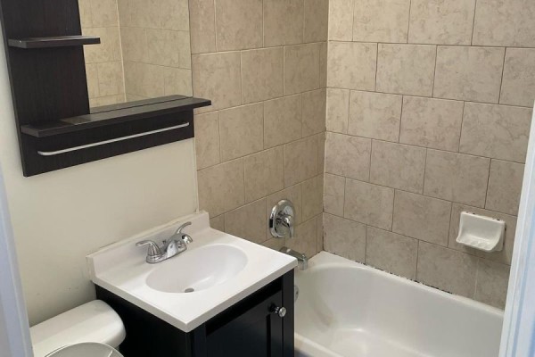 Small bathroom with beige tile walls, white toilet, white sink, and bathtub. - Lower - 78 Cavell Avenue, Toronto