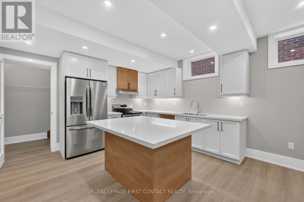 Contemporary kitchen with white quartz island, stainless steel fridge, stove, and light wood and white cabinetry. - Lower - 933 7th Line, Innisfil