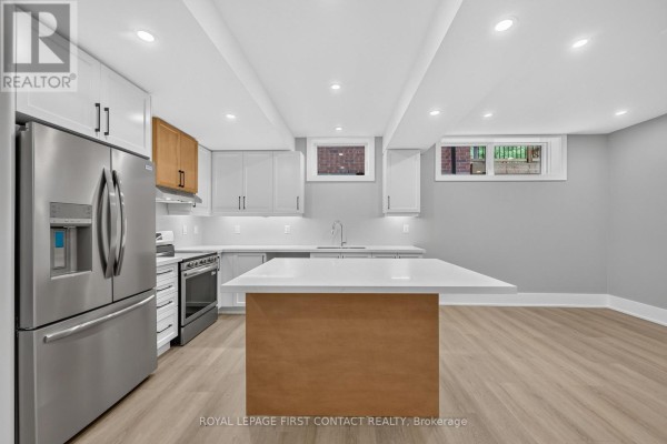 Spacious basement kitchen with light wood island, white cabinets, stainless steel appliances, and windows with brick exterior view. - Lower - 933 7th Line, Innisfil