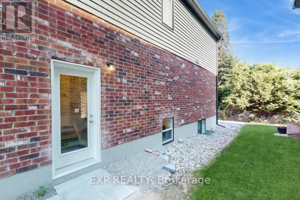 Exterior view of the house with a brick wall, a glass door, and a grassy area with landscaping. - Lower - 967 Wright Drive, Midland