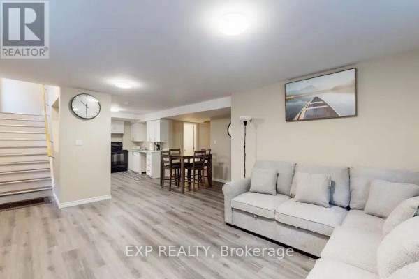 Open concept living area with a beige sectional sofa, dining table, and a kitchen with white cabinets. - Lower - 967 Wright Drive, Midland