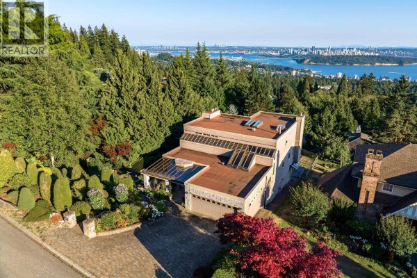 Rear exterior view of a house with large windows and a deck, surrounded by trees. - Lower 2426 Westhill Court, West Vancouver