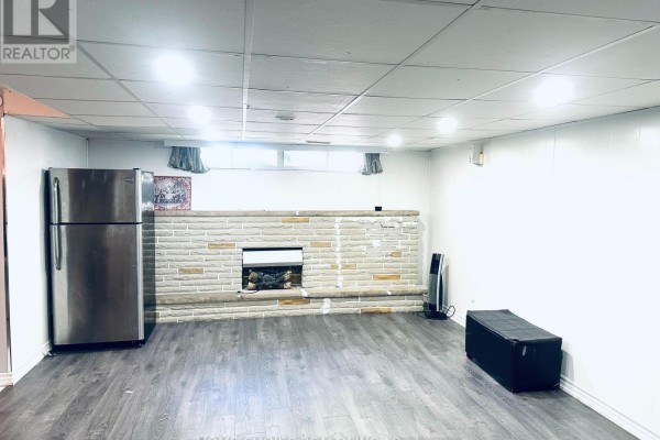 Spacious lower level room with a fireplace, stainless steel refrigerator, and dark wood laminate flooring. - Lower Level - 130 Earnscliffe Circle, Brampton