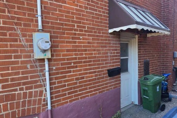 Exterior wall of a red brick house with a white meter and a closed white door. - Lower Level - 15 North Bonnington Avenue, Toronto
