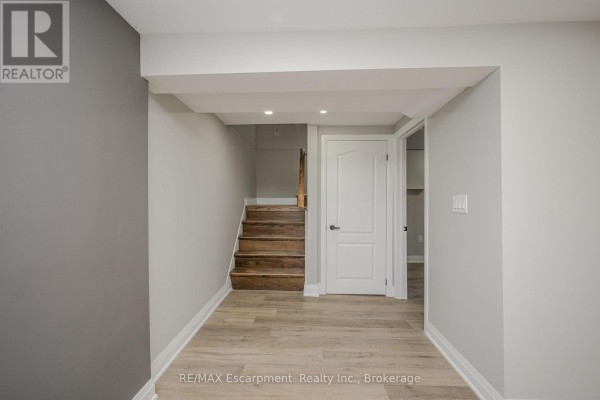 Hallway inside the lower unit with wood-look flooring and a door to the stairs. - Lower Unit - 144 East 44th Street, Hamilton
