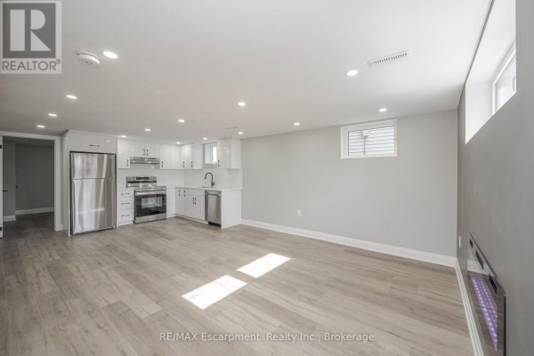 Open concept living area with a modern kitchen, stainless steel appliances, and light grey walls. - Lower Unit - 144 East 44th Street, Hamilton