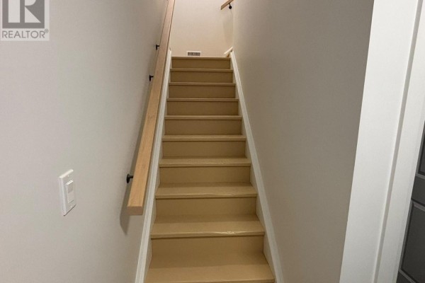 Interior view of a light-colored staircase with a wooden handrail against a beige wall. - Lower Unit - 3944 Campbell Street N, London South