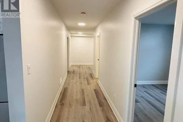 Long hallway with light wood-look flooring, white baseboards, and doors leading to rooms. - Lower Unit - 3944 Campbell Street N, London South