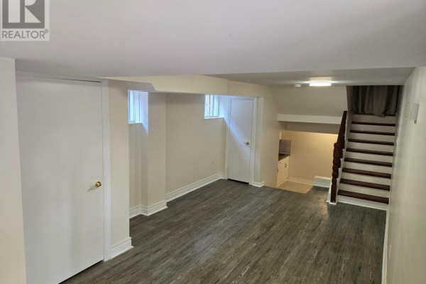 Basement living area with wood-look flooring, white doors, and staircase to kitchen. - Lower Unit - 57 Mentor Boulevard, Toronto