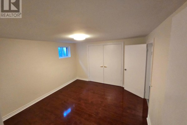 Empty basement bedroom with wood flooring, a small window, and double closet doors. - Lower Unit - 57 Mentor Boulevard, Toronto