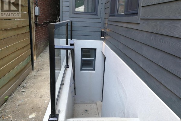 Concrete exterior stairwell leading down to a basement entrance with a glass railing and dark grey siding. - Lowunit - 246 Lippincott Street, Toronto