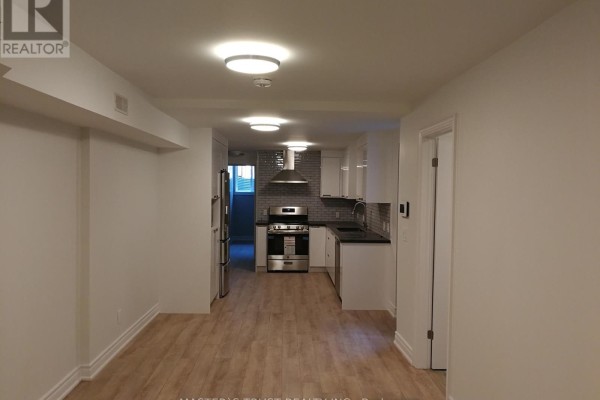 View of a modern, white kitchen with stainless steel appliances, a gas range, and light wood floors. - Lowunit - 246 Lippincott Street, Toronto