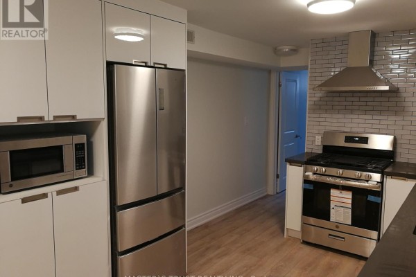 Close-up of a stainless steel refrigerator and microwave in a white kitchen with grey subway tile backsplash. - Lowunit - 246 Lippincott Street, Toronto