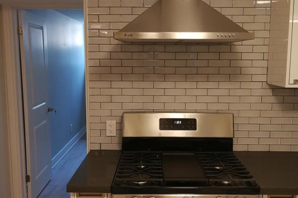 Detail of a stainless steel gas range and range hood against a light grey subway tile backsplash in a kitchen. - Lowunit - 246 Lippincott Street, Toronto