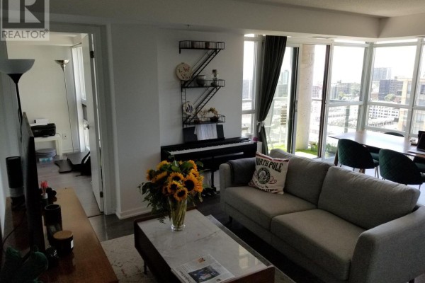 Living room with a grey sectional sofa, coffee table, and a digital piano with sunflowers. - Lp-09 - 68 Abell Street, Toronto