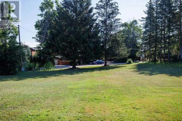 Lawn with tall evergreen trees and a paved driveway with a parked car. - Lt 14 Butternut Drive, Kawartha Lakes