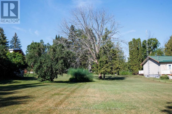 Wide grassy area with scattered trees, two small buildings, and a clear blue sky. - Lt 14 Butternut Drive, Kawartha Lakes