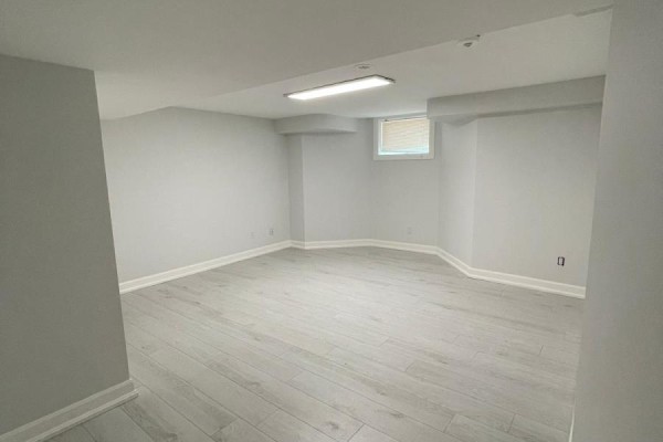 Empty, unfinished basement room with light gray walls, light wood laminate flooring, and a single ceiling light. - Lwr Lvl - 18 Reuben Avenue, Toronto