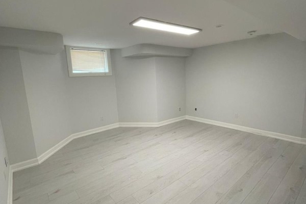 Unfinished basement room with a small window, light gray walls, and light wood laminate flooring. - Lwr Lvl - 18 Reuben Avenue, Toronto