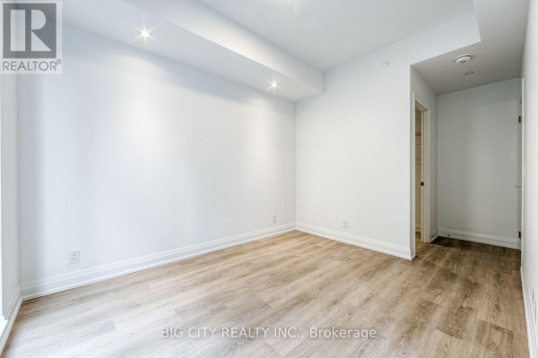 View of an empty room with light wood laminate flooring and white walls. - M05 - 36 Brentcliffe Road, Toronto