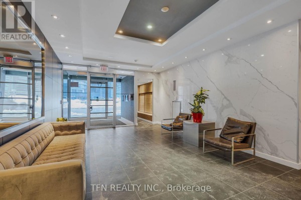 Apartment building lobby with a tan sofa, tiled floor, marble accent wall, and two chairs. - M22 - 350 Wellington Street W, Toronto