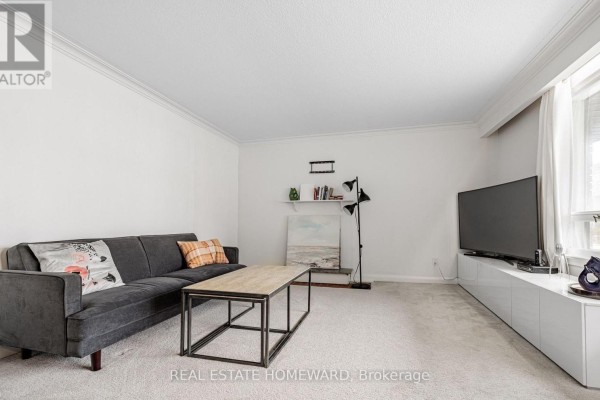 Living room with a dark gray sofa, coffee table, and a television on a white media console. - Main - 11 Greenbriar Road, Toronto
