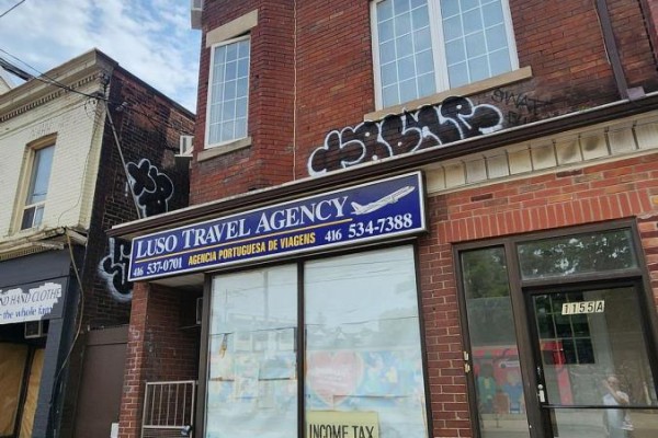 Close-up of the Luso Travel Agency sign and the building's brick facade with graffiti. - Main - 1155 Dundas Street W, Toronto