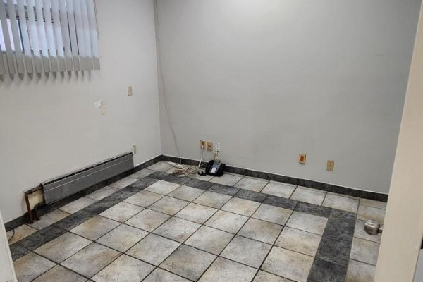 Empty room with tiled floor, heating unit, blinds, and electrical outlets. - Main - 1155 Dundas Street W, Toronto
