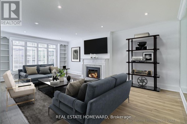 Living room with a fireplace, television, large windows, and seating arranged on a wooden floor. - Main - 12 Highbourne Road, Toronto