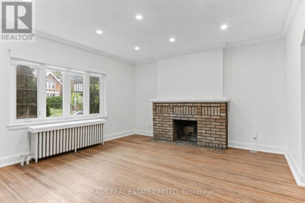 Living room with hardwood floors, a brick fireplace, and a large bay window. - Main - 121 Braemar Avenue, Toronto